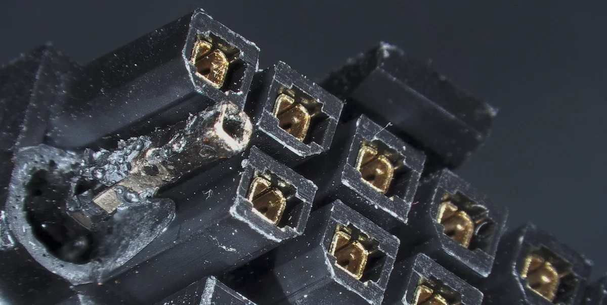 Close-up of heat-damaged black GPU power connector housing and exposed metal terminals